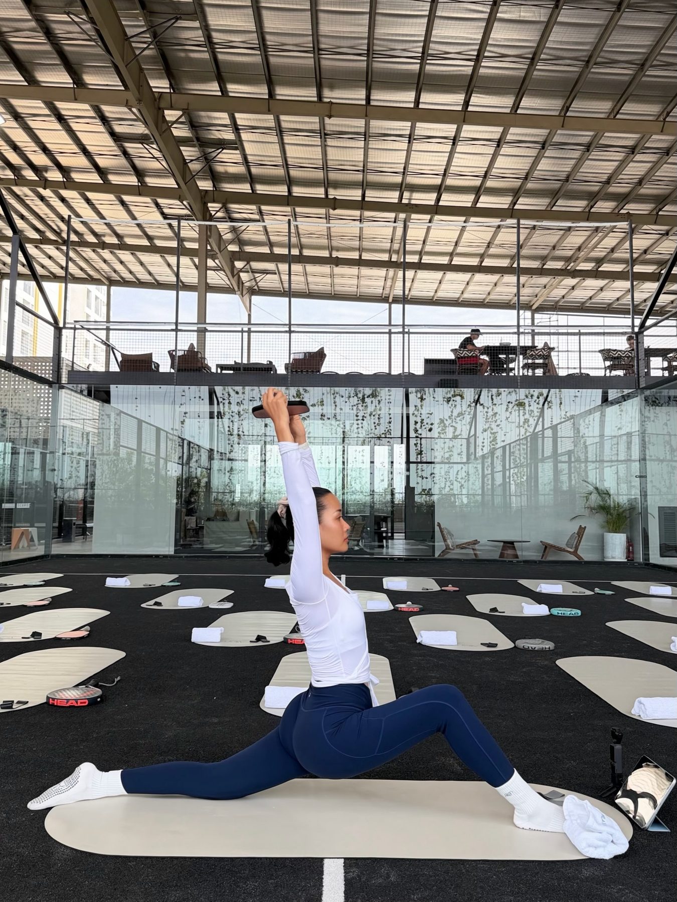 Pisey in a lunge on a mat at an outdoor court, arms raised, Phnom Penh rooftops behind